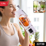 A smiling woman in a light sports bra sips from a white portable blender filled with orange juice and berries.
