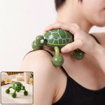 A person's hand guides a green turtle-shaped massager with four rolling feet across their shoulder, providing relief.
