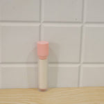 A pink and white lint roller with its clear ribbed protective case stands upright on a wooden surface against a white tiled