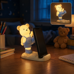 A glowing yellow bear phone holder with blue overalls on a desk at night, holding a phone.