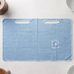 Flat lay of a light blue rectangular bath towel wrap with two armholes and a small pocket with an R monogram.