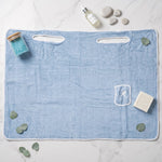 Flat lay of a light blue bath towel wrap surrounded by bath salts, essential oil, soap, and eucalyptus leaves.