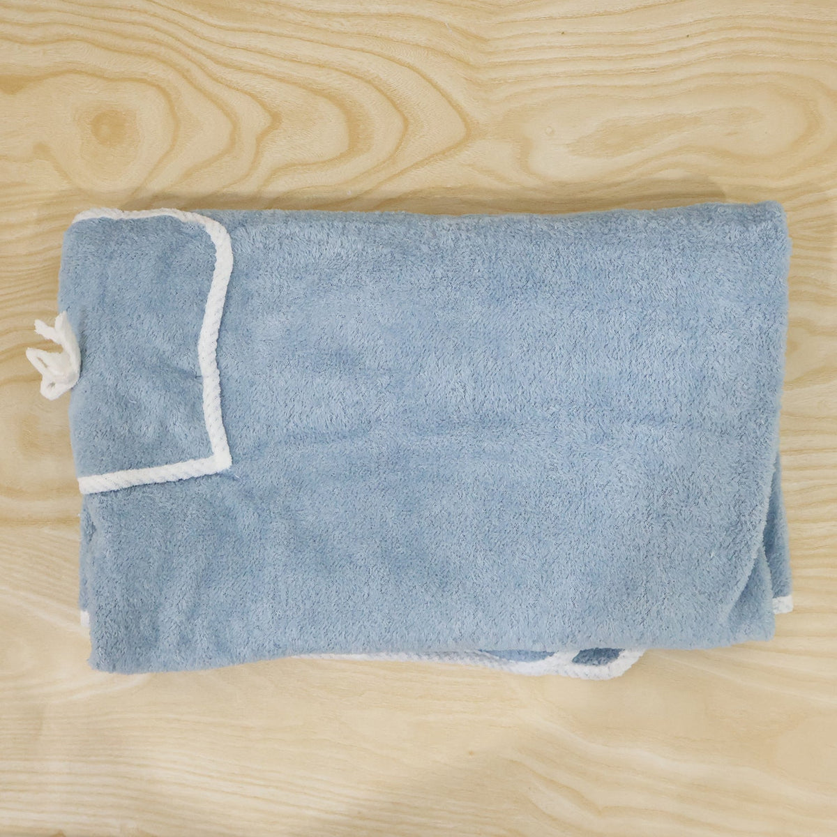 Folded light blue bath towel wrap with white trim and a small pocket, laid on a light wooden surface.