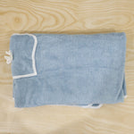 Folded light blue bath towel wrap with white trim and a small pocket, laid on a light wooden surface.