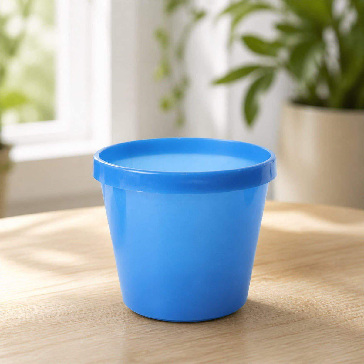 A single blue plastic planter pot sits on a light wooden surface in a bright room.