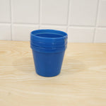 A stack of three blue plastic planter pots sits on a light wood surface against a tiled wall.