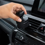 A hand uses the black detailing brush to clean a car's air conditioning vent on the dashboard.