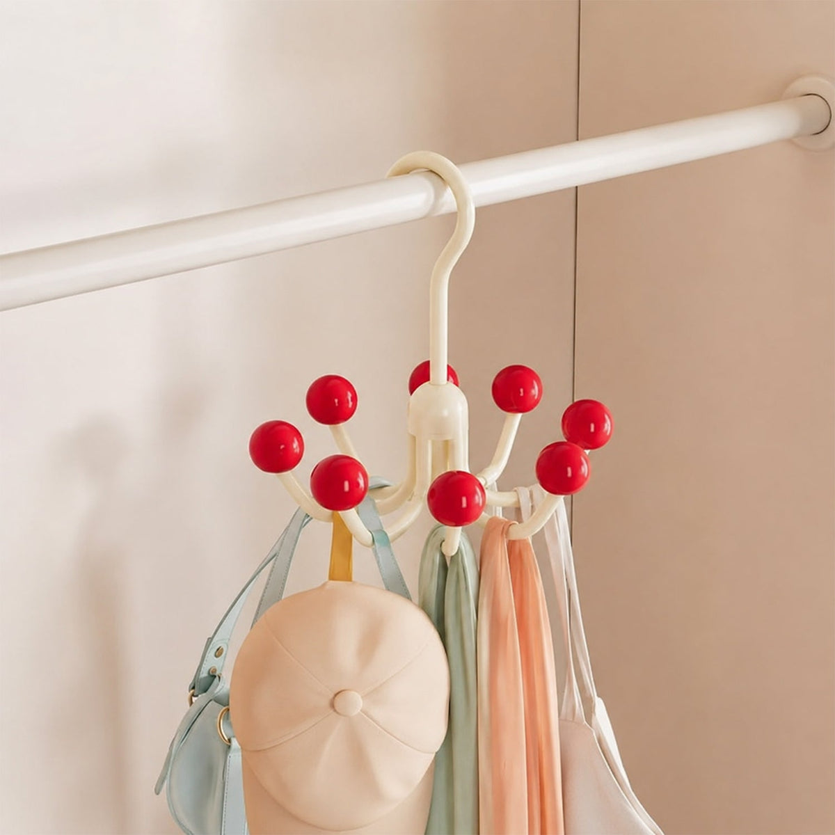 A cream multi-hook hanger with red ball tips, holding a light blue bag, a beige cap, and two scarves, hanging inside a white