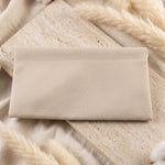 A cream textured faux leather pouch lying flat on a light-colored textured surface with white fluffy decorative elements.
