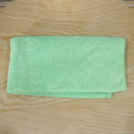 A light green microfiber towel with embossed heart and flower patterns, folded on a light wooden surface.