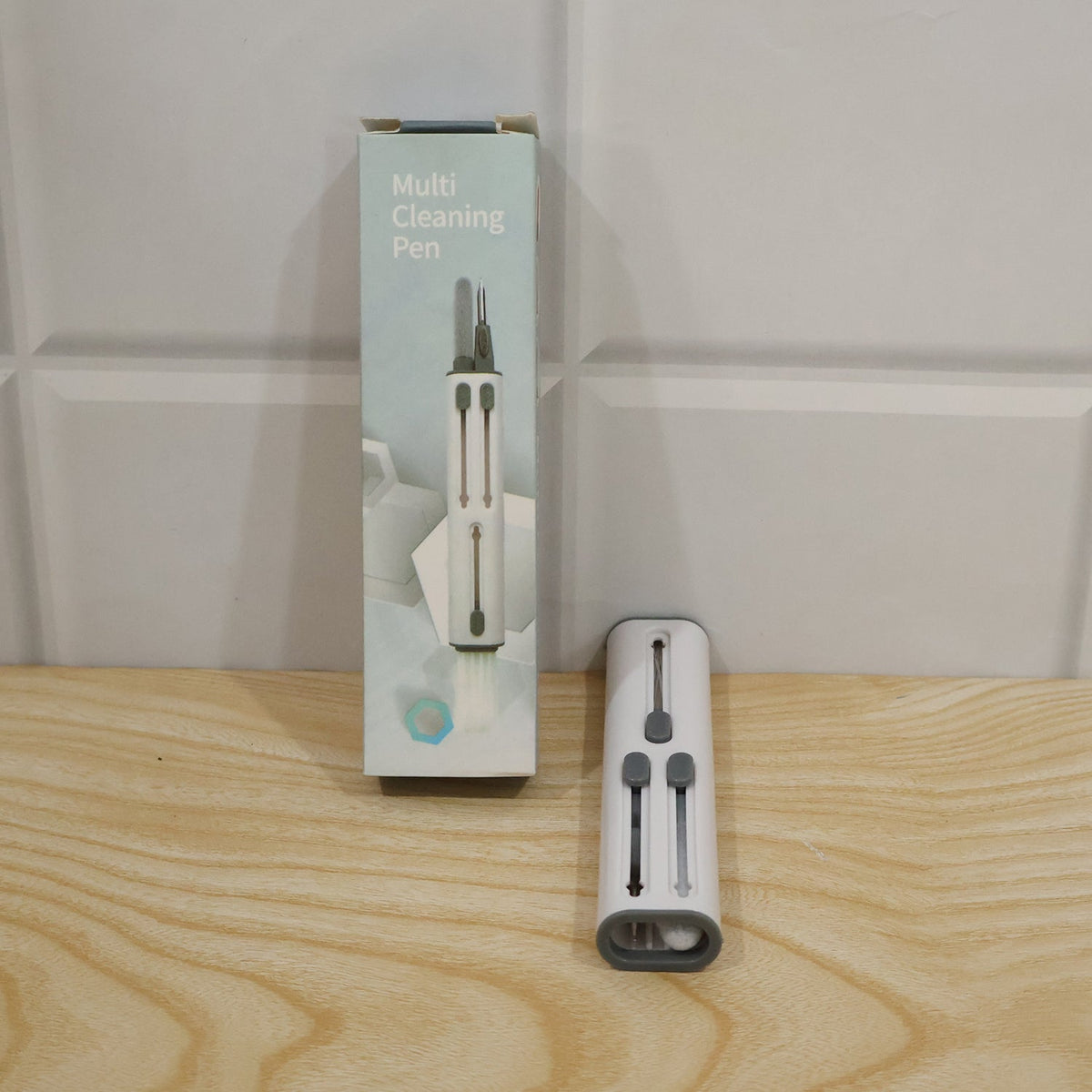 The multi-tool cleaning pen next to its light blue and white retail packaging on a wooden surface.