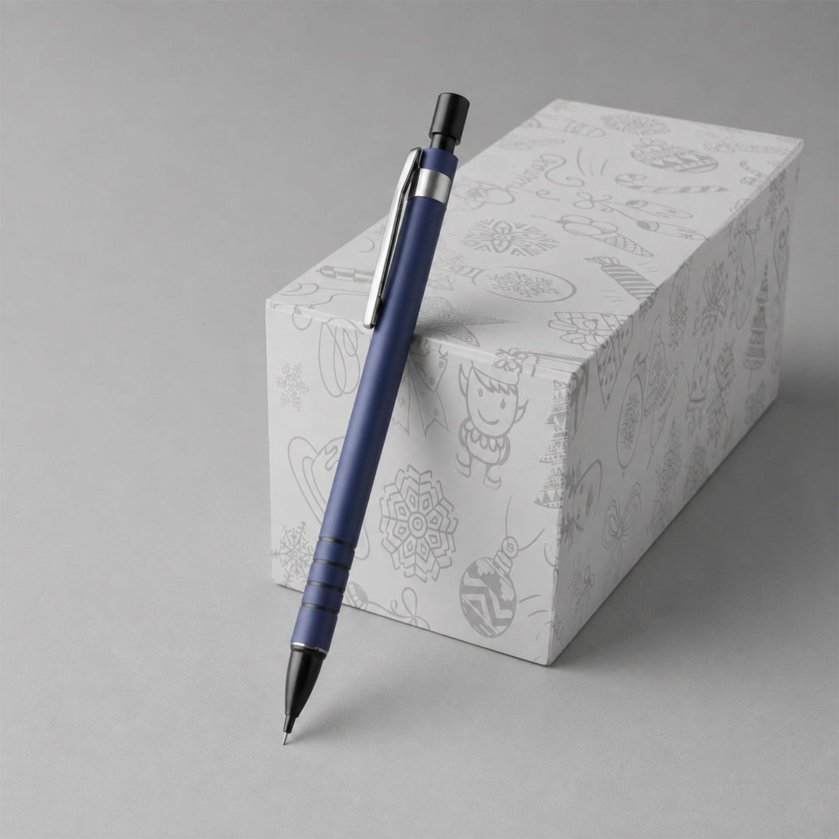 A blue mechanical pencil leans against a white gift box with festive line art designs on a gray background.