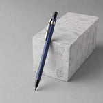 A blue mechanical pencil leans against a white gift box with festive line art designs on a gray background.