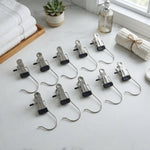 Ten metal clip hangers with black rubber tips are spread out on a white marble counter, with neatly folded white towels and