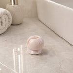 A single white toothbrush holder clip with water droplets on a light grey marble countertop next to a white sink and a