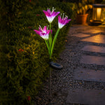 A single purple and white solar flower stake light illuminates a garden pathway at dusk. – view 8