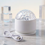 A white LED projection light with a clear textured dome and a white USB cable on a marble surface with clear blocks.