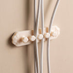 A beige self-adhesive cable organizer clip with five flower-shaped holders securing three white cables on a beige wall.