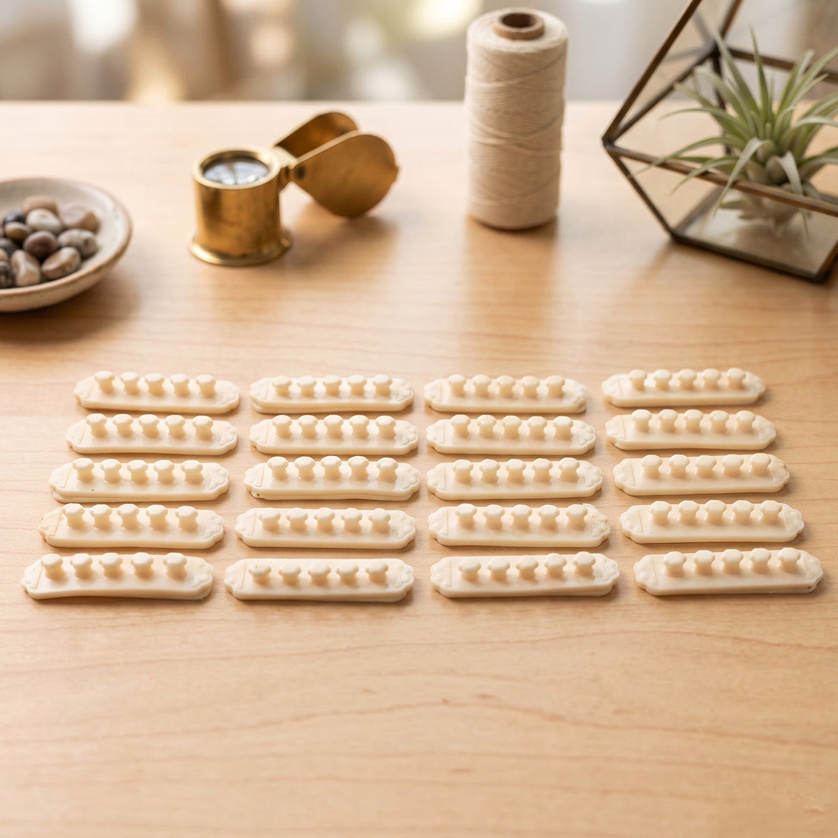 Twenty beige self-adhesive cable organizer clips, each with five flower-shaped holders, arranged on a light wooden table