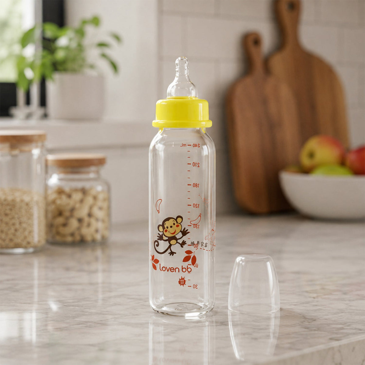 A clear glass baby bottle with a yellow nipple and monkey design sits on a speckled kitchen counter.
