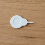 A small white plastic tool with a circular base and a pointed end rests on a light brown wooden surface.