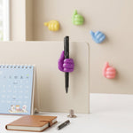 A purple thumbs-up clip holds a black pen on a desk divider, with other colourful clips on the wall in the background.