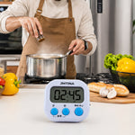 A white digital kitchen timer with blue buttons sits next to its white packaging box on a light wooden surface.