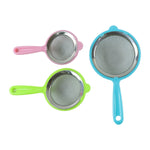 Three strainers in pink, green, and blue with plastic handles and stainless steel mesh are arranged on a white background.