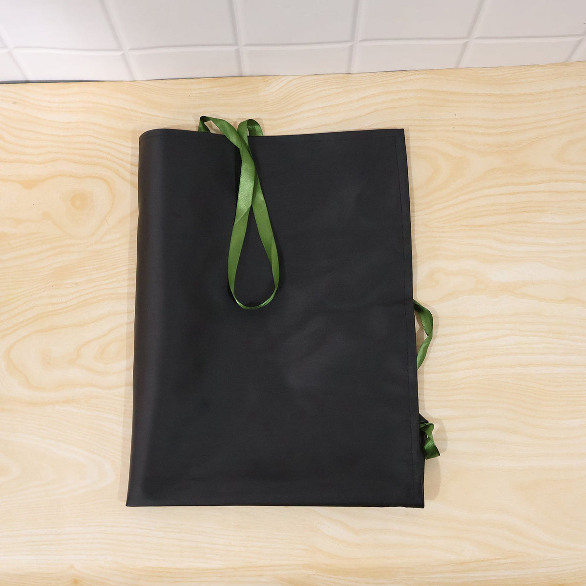 A black apron with green ties is folded neatly on a light wooden surface.