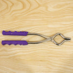 A stainless steel pot lifter with purple handles lying on a light wooden surface.