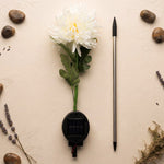The disassembled white chrysanthemum solar light components laid out on a textured beige surface with decorative stones and