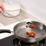 A hand using the stainless steel tongs to turn fried chicken pieces in a silver frying pan on a stove.