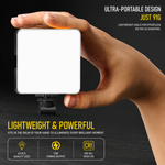 A hand holding a small, illuminated square LED video light with a white diffuser, against a dark background.