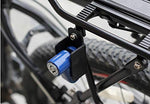 A blue wheel security device is attached to a bicycle's rear rack, with a tire and spokes visible in the background.