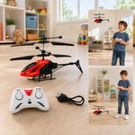 A red and black toy helicopter with a white remote control and USB charging cable on a wooden floor, with a child playing in