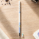 A white and blue pen refill with a small light blue cap on a wooden desk, surrounded by dried lavender.