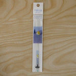 A white and blue pen refill in clear plastic packaging with a cartoon house design, lying on a wooden surface.