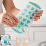 A person's hands gently twist a clear and teal heart-shaped ice cube tray, releasing two heart-shaped ice cubes into a glass