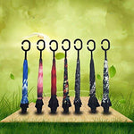Seven closed reverse umbrellas with C-shaped handles stand upright on a wooden board against a green, leafy background.