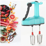 A turquoise manual hand blender with black handle and red-tipped whisks is shown next to a colorful arrangement of fresh