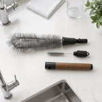 The three parts of the cleaning brush set are neatly arranged on a white kitchen counter next to a sink.