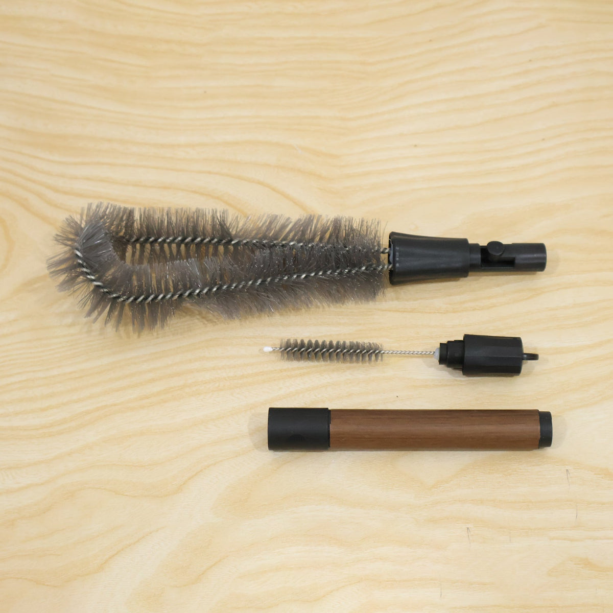 The three components of the cleaning brush set are displayed disassembled on a light wooden surface.