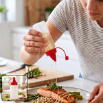 A person drizzles oil from a clear plastic squeeze bottle with a red cap onto salmon and asparagus.