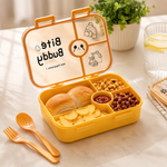 Open yellow 4-compartment lunch box filled with bread, chips, peanuts, and ketchup, with orange cutlery beside it.