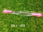 A pink and silver facial hair remover spring tool in clear plastic packaging on a green grass-like surface with text 'DD =