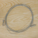 A long, silver stainless steel wire rope with two carabiner hooks is laid out on a light wooden surface.