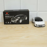 A black box labeled 'XINGDIAN PHONE HOLDER' sits next to a white car-shaped phone holder on a wooden surface.
