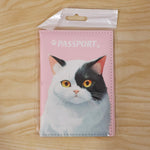 The pink passport holder with a cat design is presented in clear plastic packaging against a light wooden background.