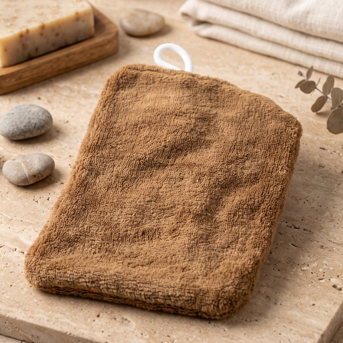 The plain brown back of a rectangular microfiber towel with a white hanging loop rests on a tiled surface with soap and