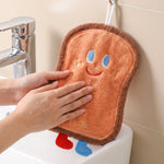 A person's hands drying on a brown cartoon bread slice towel hanging over a white sink.